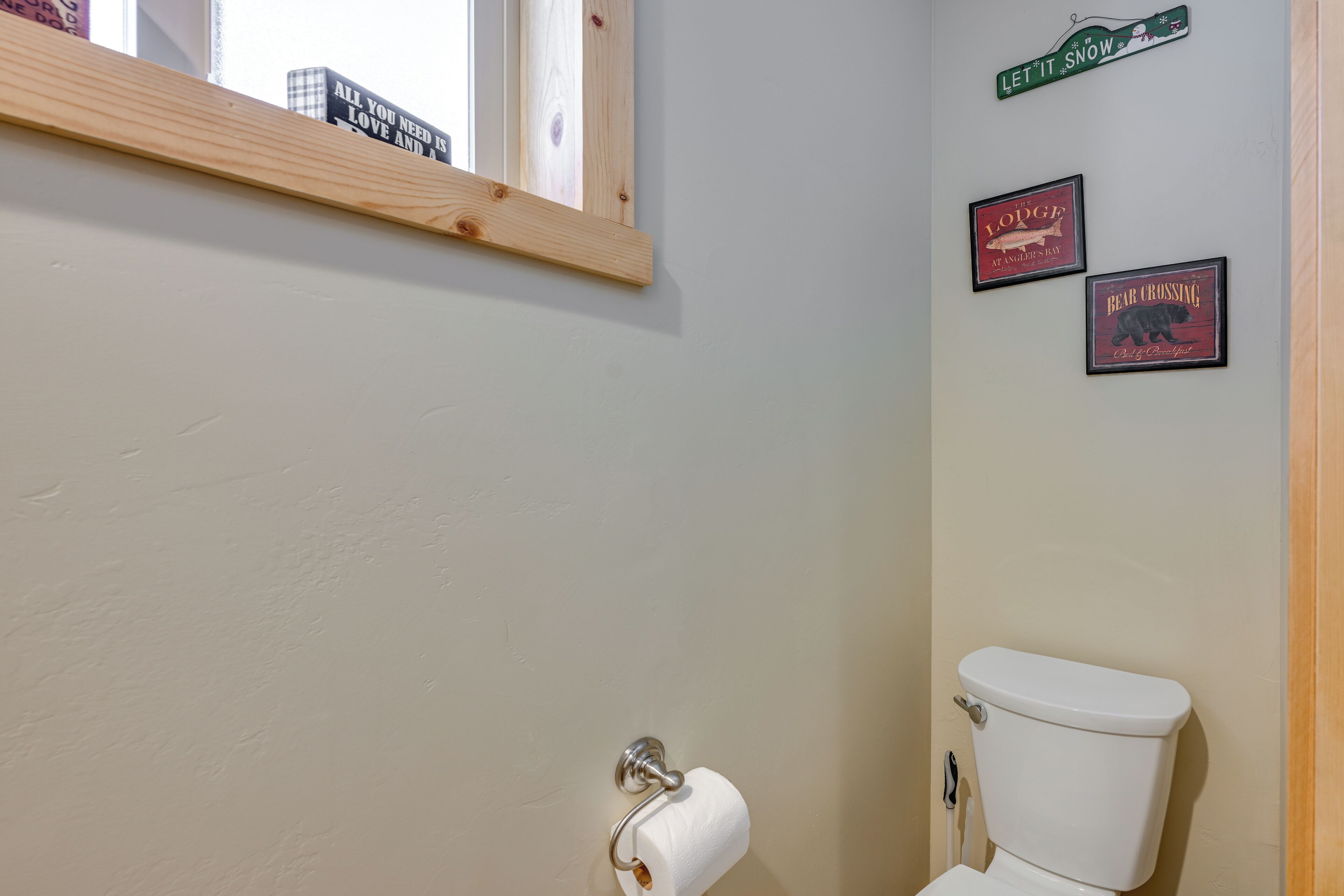 Ein Badezimmer mit Toilette, einer Holzablage und drei gerahmten Schildern an der Wand.