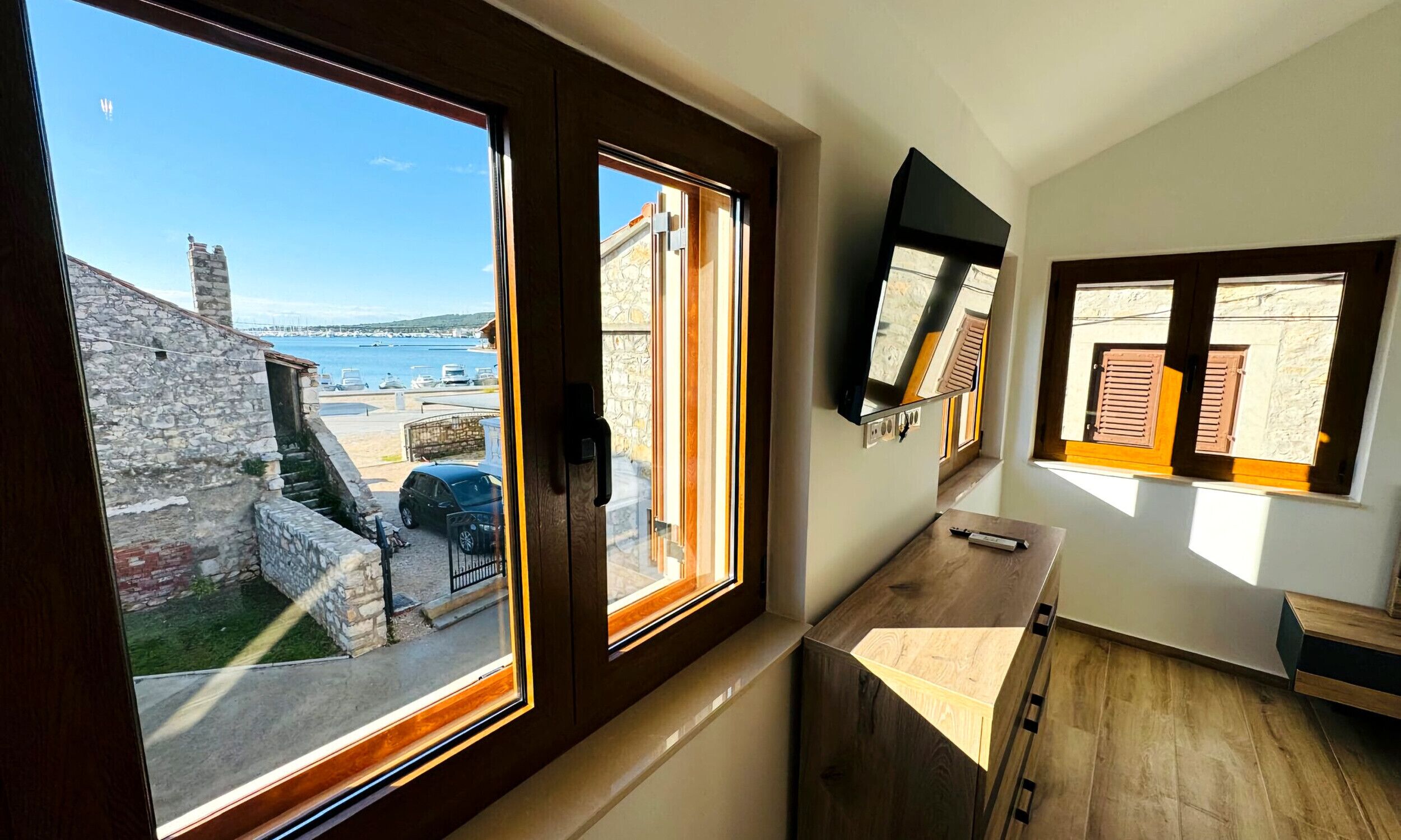 A room with a large bay window overlooking a marina and stone buildings.