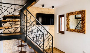 A modern staircase with a geometric metal railing, a flat-screen TV mounted on the wall, and a decorative mirror with a patterned frame.