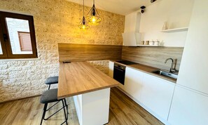 A modern kitchen with a wooden island, white cabinets, and a stone wall backsplash.