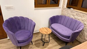 Dos sillones morados con una pequeña mesa de madera entre ellos, una pared blanca y una puerta de madera.