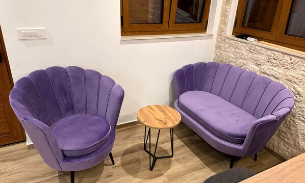 Two purple armchairs with a small wooden table between them, a white wall, and a wooden door.
