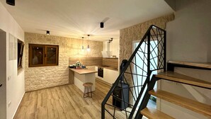 Una cocina moderna con un salpicadero de pared de piedra, piso de madera, una isla central con taburetes de bar y una escalera con barandilla de metal.
