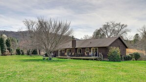 A rustic cabin with a deck, surrounded by a grassy yard and trees.