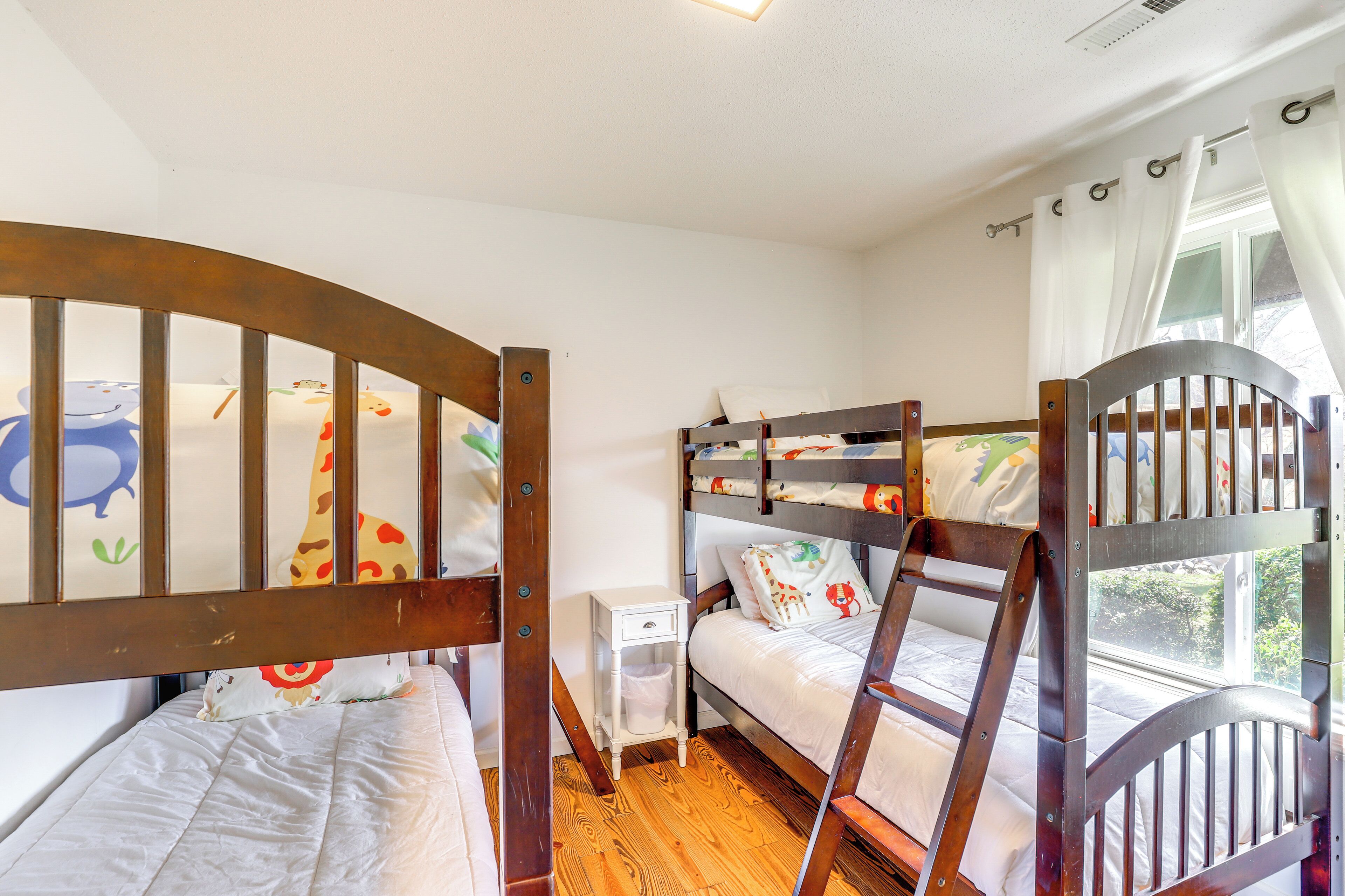 A room with bunk beds, a small bedside table, and a window with curtains.