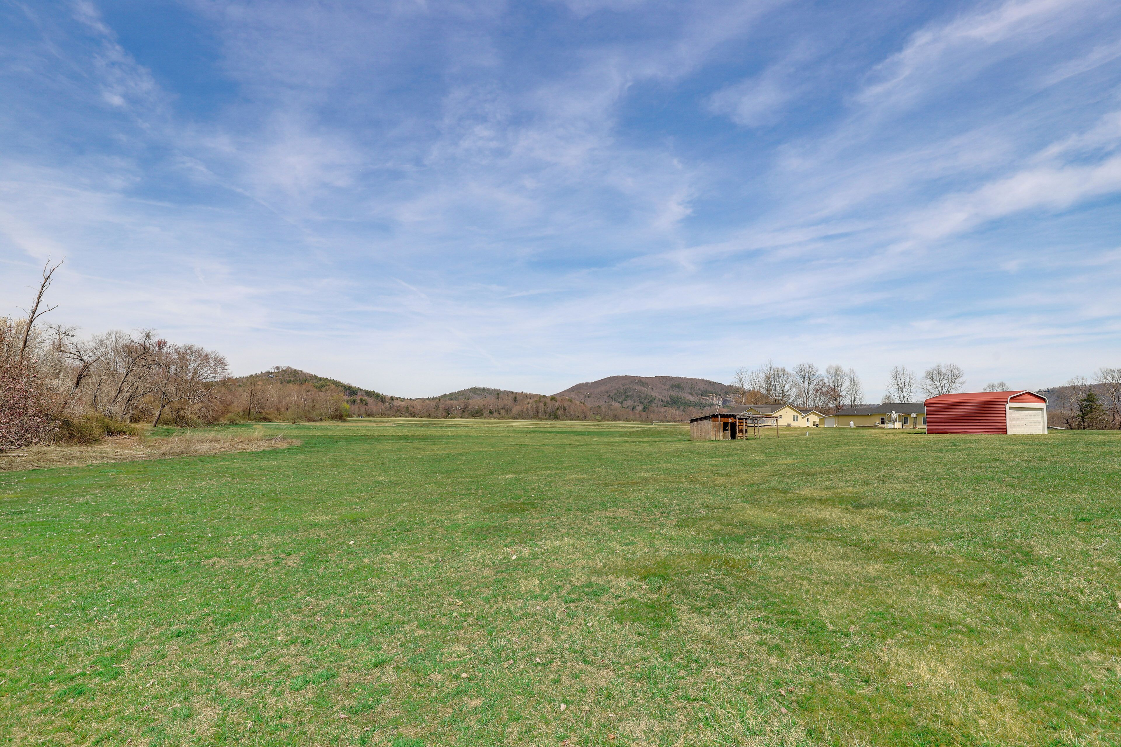 A spacious grassy field with a red barn and a small shed in the distance, surrounded by hills and sparse trees.
