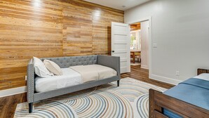 A bedroom with a grey sofa bed, a patterned rug, and wooden paneling on the wall. - Furnished Deck + Views: Rural Schulenburg Retreat (Schulenburg)