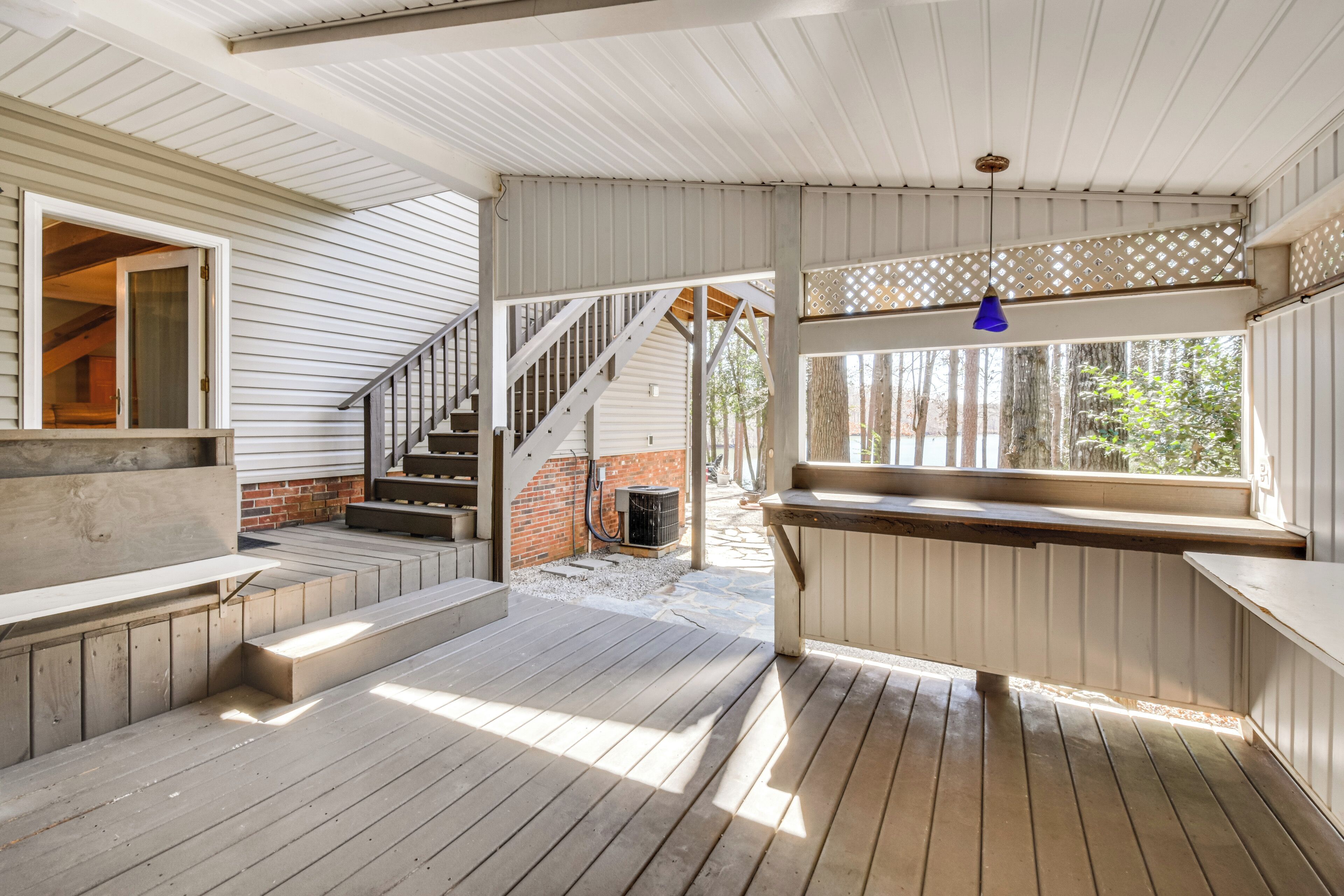 Un espace extérieur abrité, doté d’un plancher en bois, d’un escalier et d’une fenêtre donnant sur la verdure.