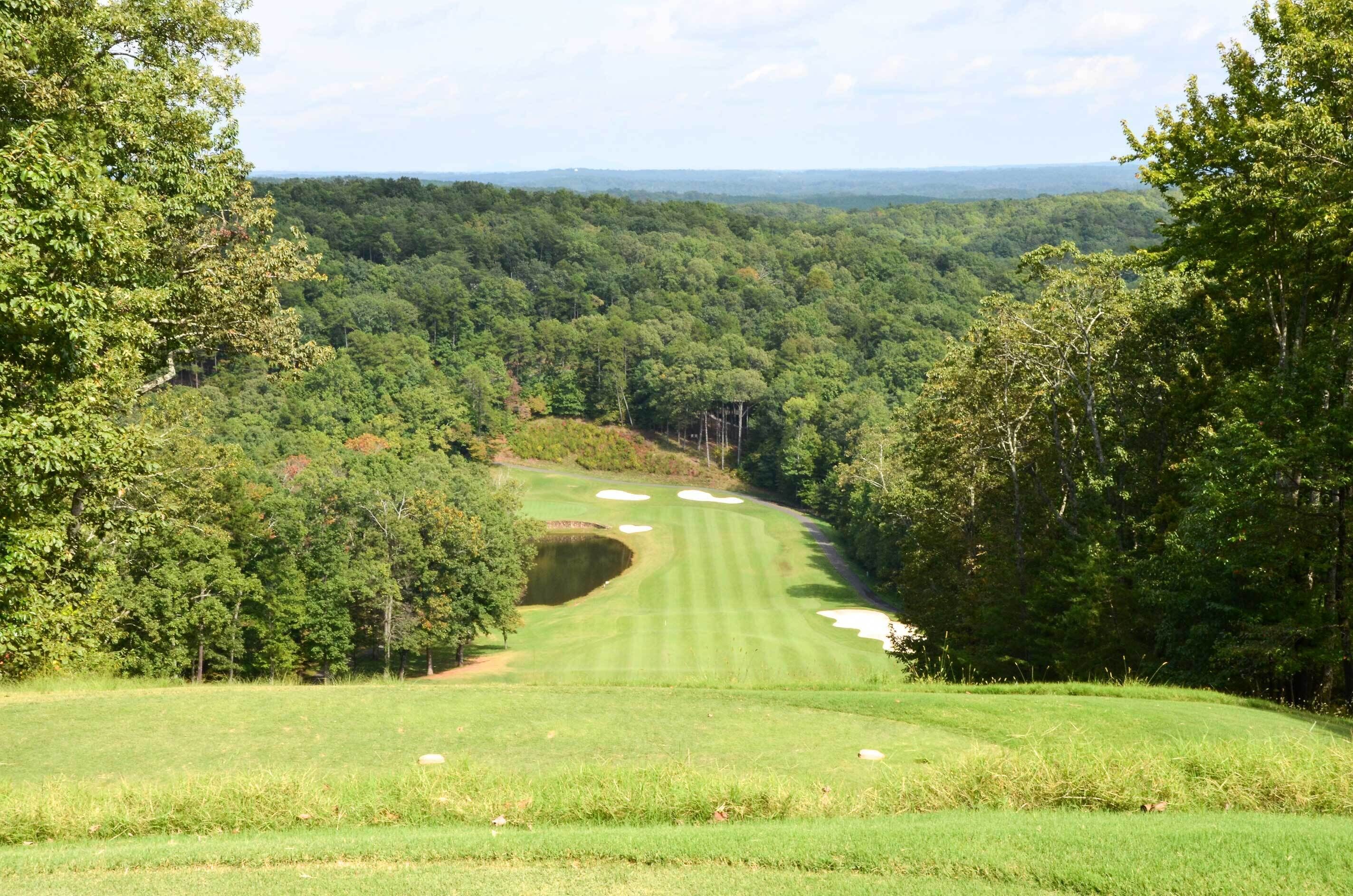 A golf course with a clear view of the fairway, sand bunkers, and surrounding forest.