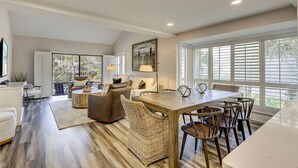 A spacious living area with a dining table, comfortable seating, and large windows.