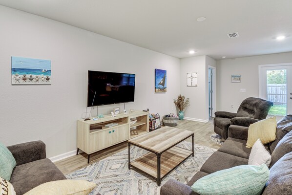 A living room with a TV, wooden entertainment unit, brown leather sofa, and patterned rug. - 6 Mi to Gulf Shores Beach: Family Getaway! (Foley)