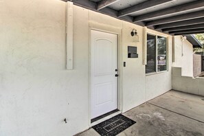 A white door with a doormat, a small window, and a wall-mounted light fixture. - Charming Home ~ 7 Mi to Downtown Tucson! (Tucson)