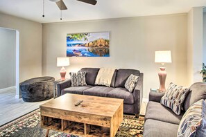 A living room with a gray sofa, two side tables with lamps, a wooden coffee table, and a large landscape painting on the wall. - Charming Home ~ 7 Mi to Downtown Tucson! (Tucson)