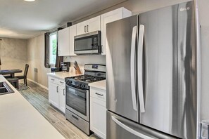 A modern kitchen with white cabinets, a stainless steel refrigerator, a microwave, a stove, and a sink. - Charming Home ~ 7 Mi to Downtown Tucson! (Tucson)