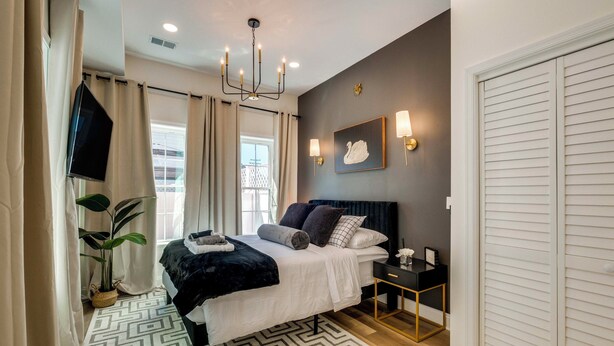 A modern bedroom with a bed, bedside tables, a TV, and a large window with curtains.