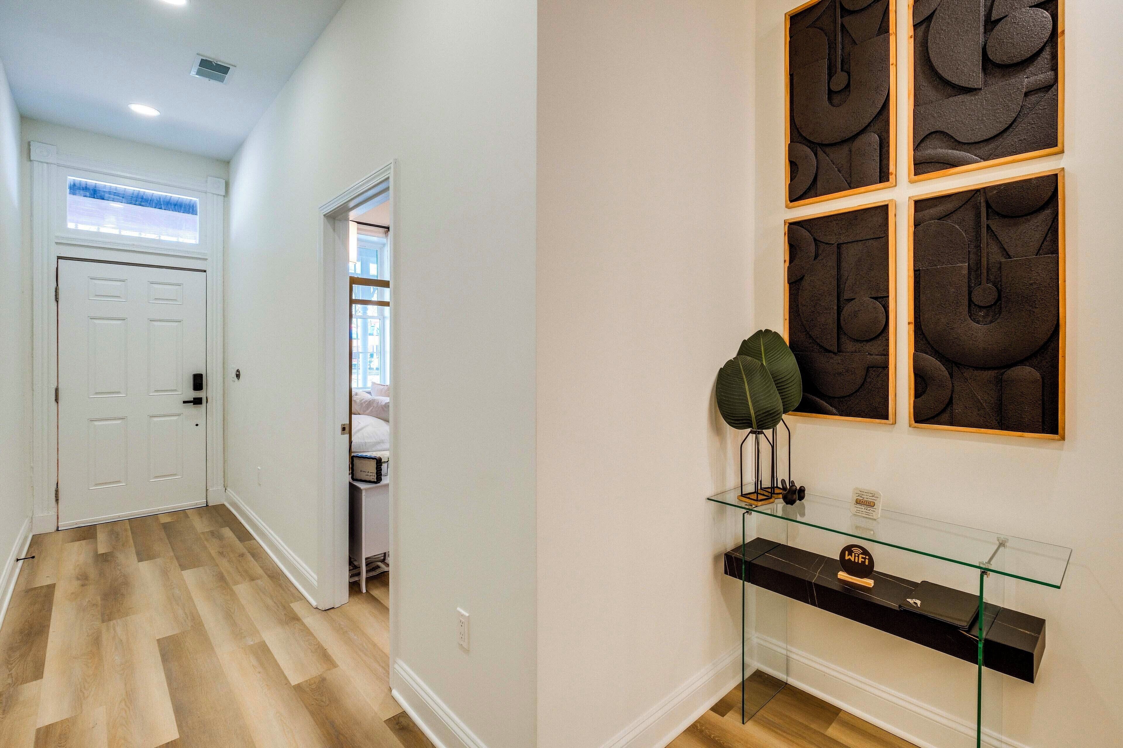 A hallway with a wooden floor, a white door, and a glass console table with a sign.