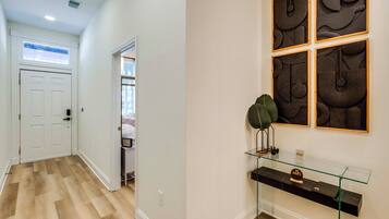 A hallway with a wooden floor, a white door, and a glass console table with a sign.