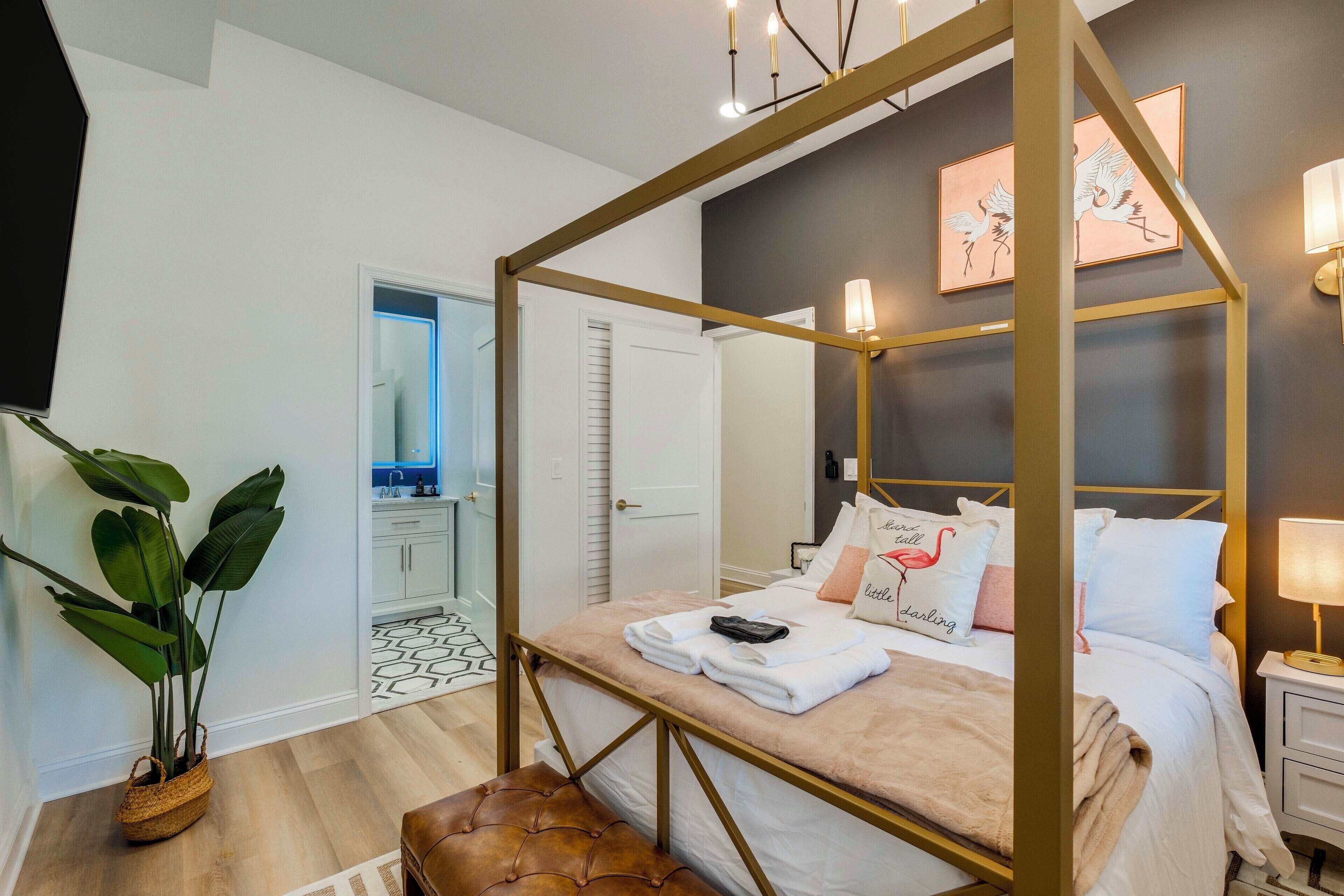 A four-poster bed with a gold frame, a bedside lamp, and a potted plant.