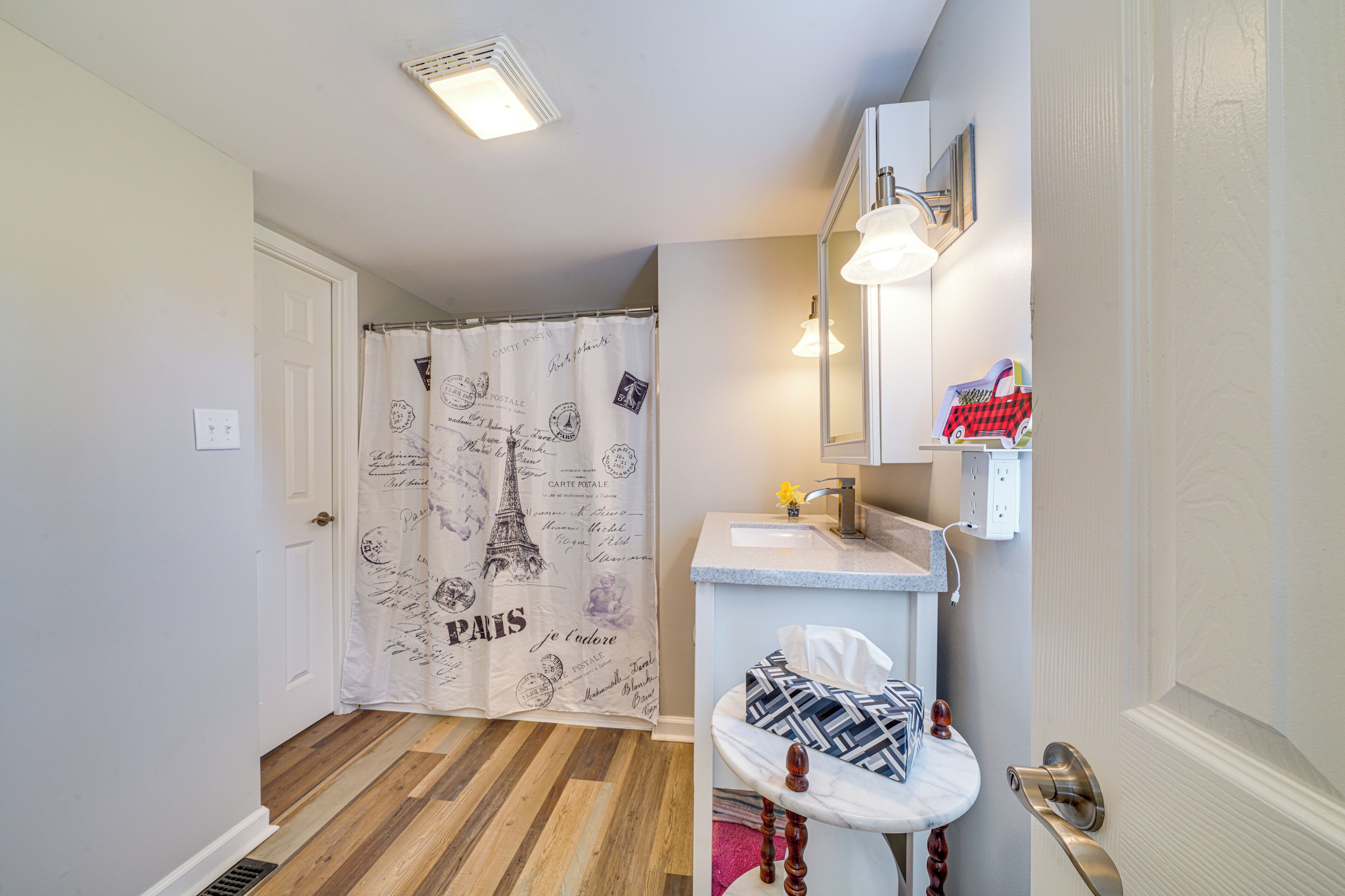 A bathroom with a shower curtain featuring Parisian designs, a sink with a mirror, and a small shelf with a toy car.