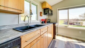 A modern kitchen with wooden cabinets, a black sink, and a microwave. - 3 Mi to Caesars Casino: Indiana Retreat w/ Patio! (New Albany)