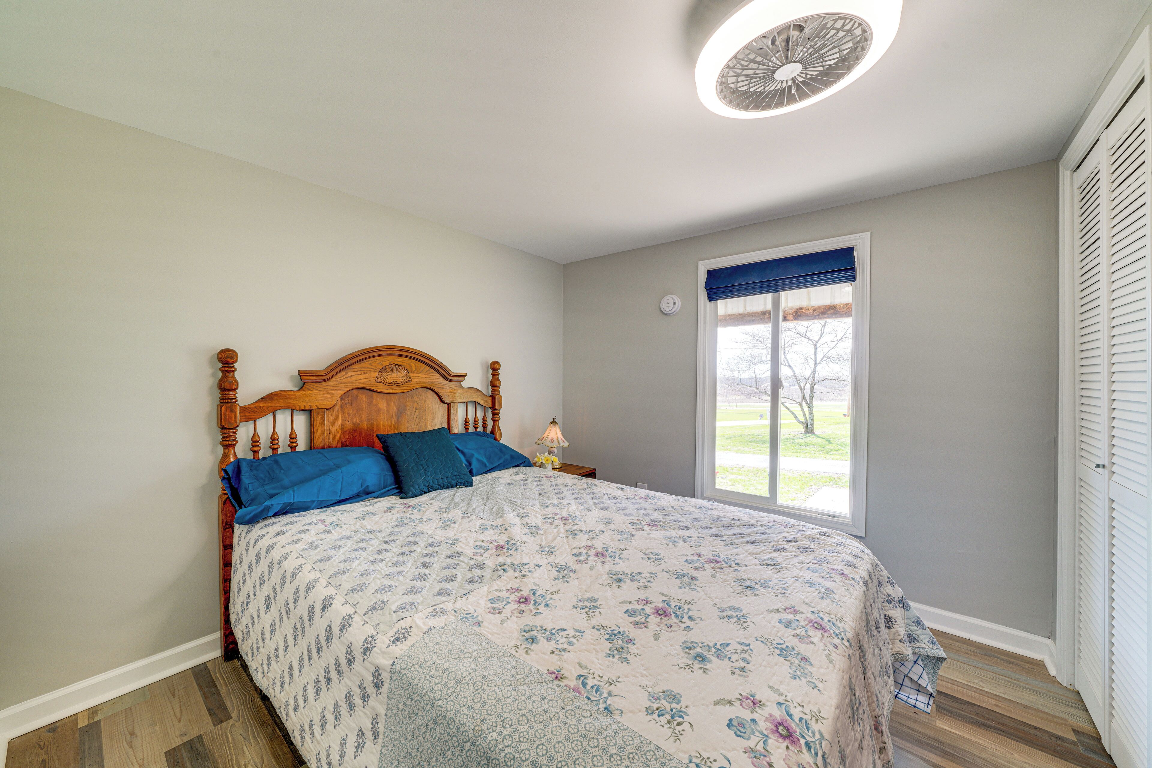 A bedroom with a wooden bed, a window with a view, and a ceiling fan.