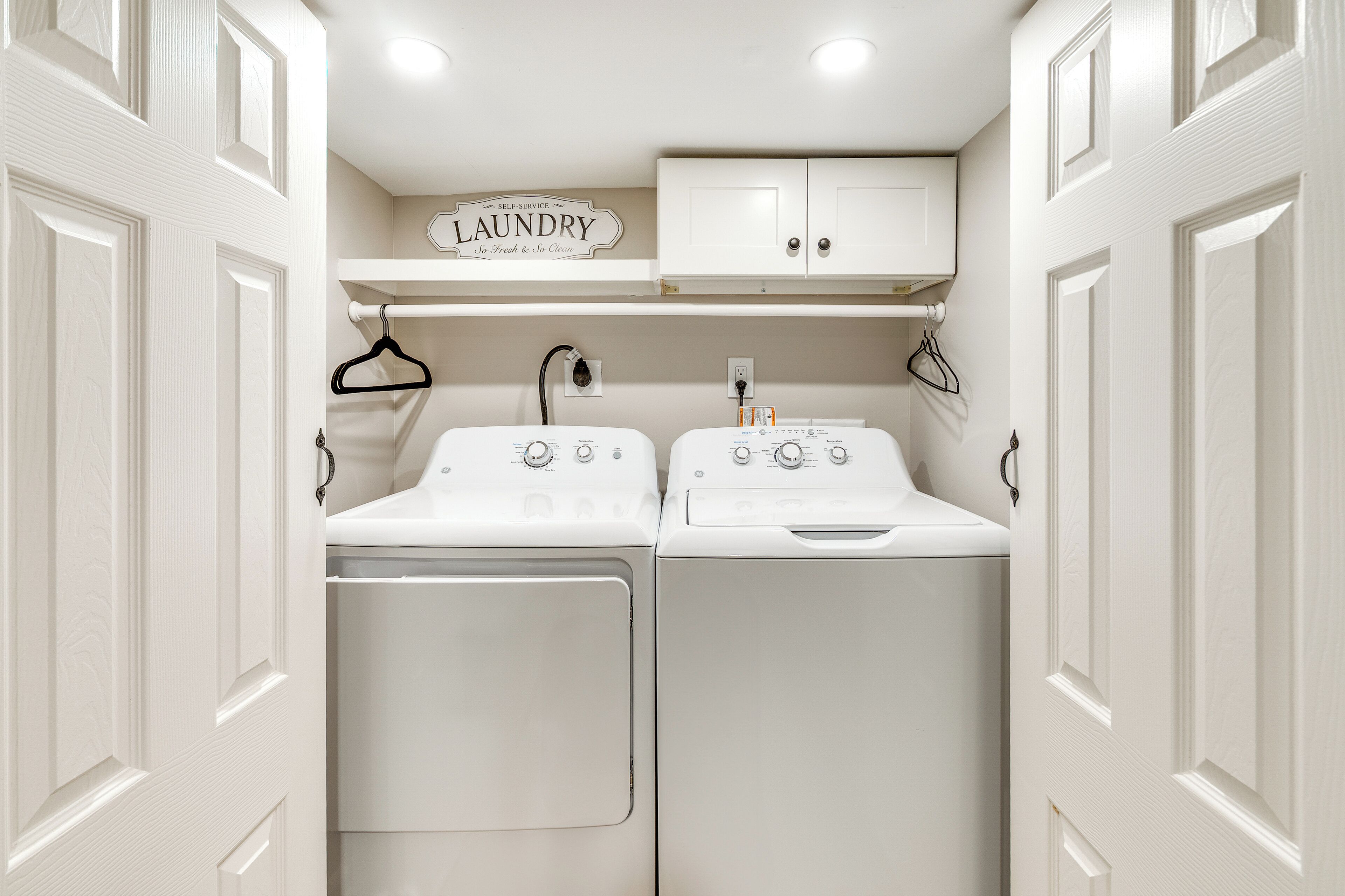 A laundry room with two washing machines, a dryer, and a shelf above with a sign that says "LAUNDRY".