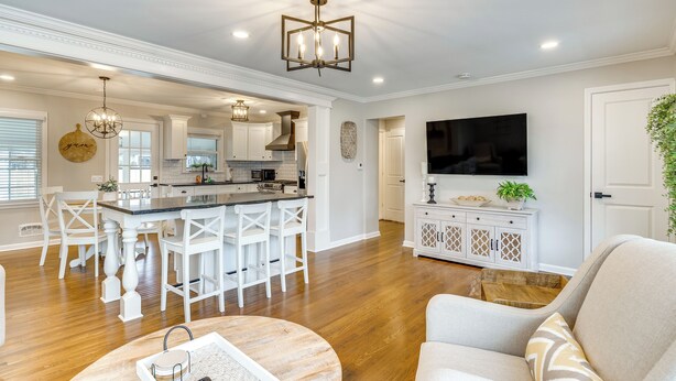 A spacious living room with a large TV, a dining area with white chairs, and a kitchen with a central island. - Screened Patio & Fire Pit: Modern Westerville Home (Westerville)