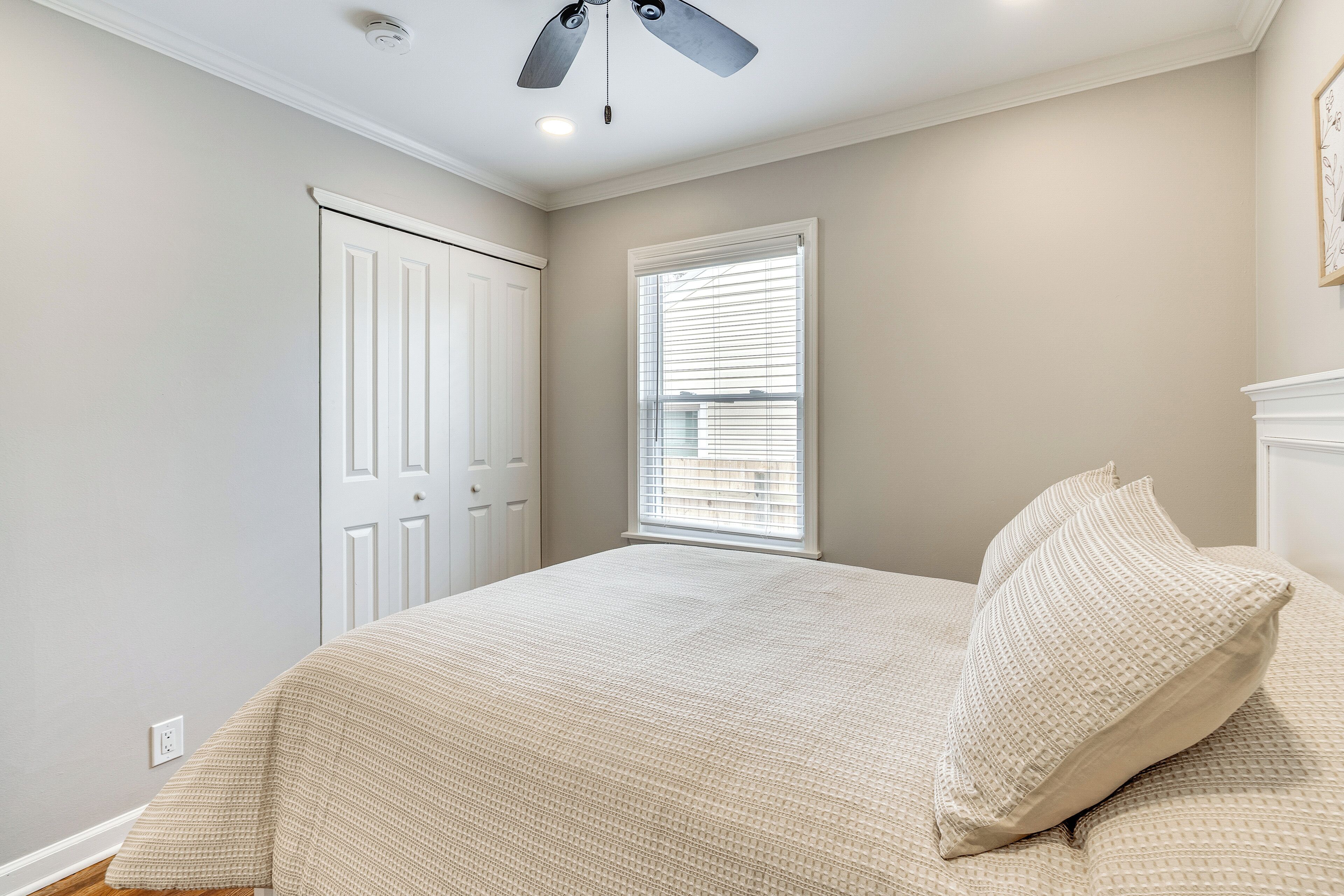 Une chambre à coucher avec un lit, un ventilateur de plafond, une fenêtre avec des stores et une porte.