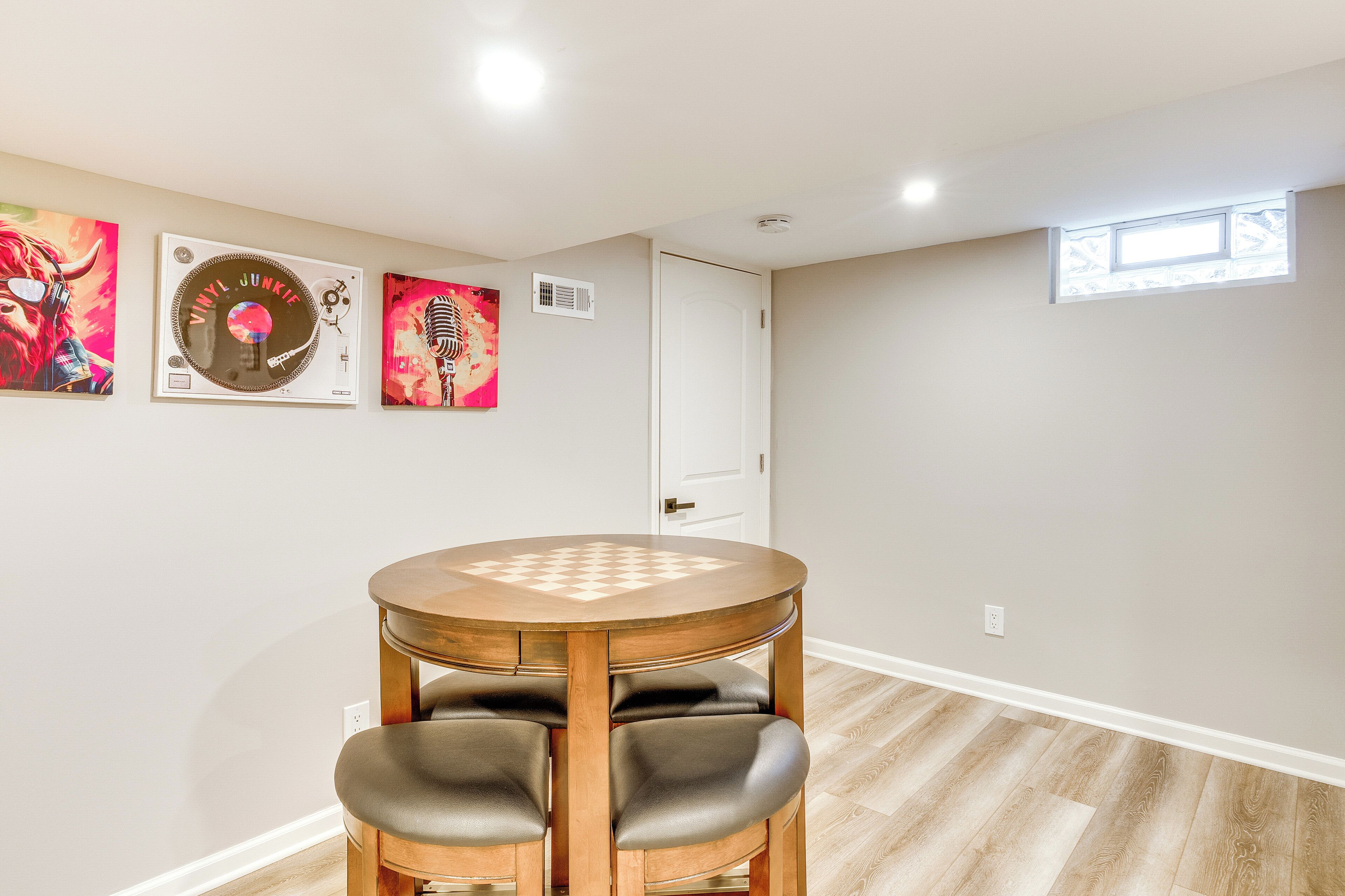 A room with a round wooden table and two chairs, a white door, and three wall-mounted vinyl records.