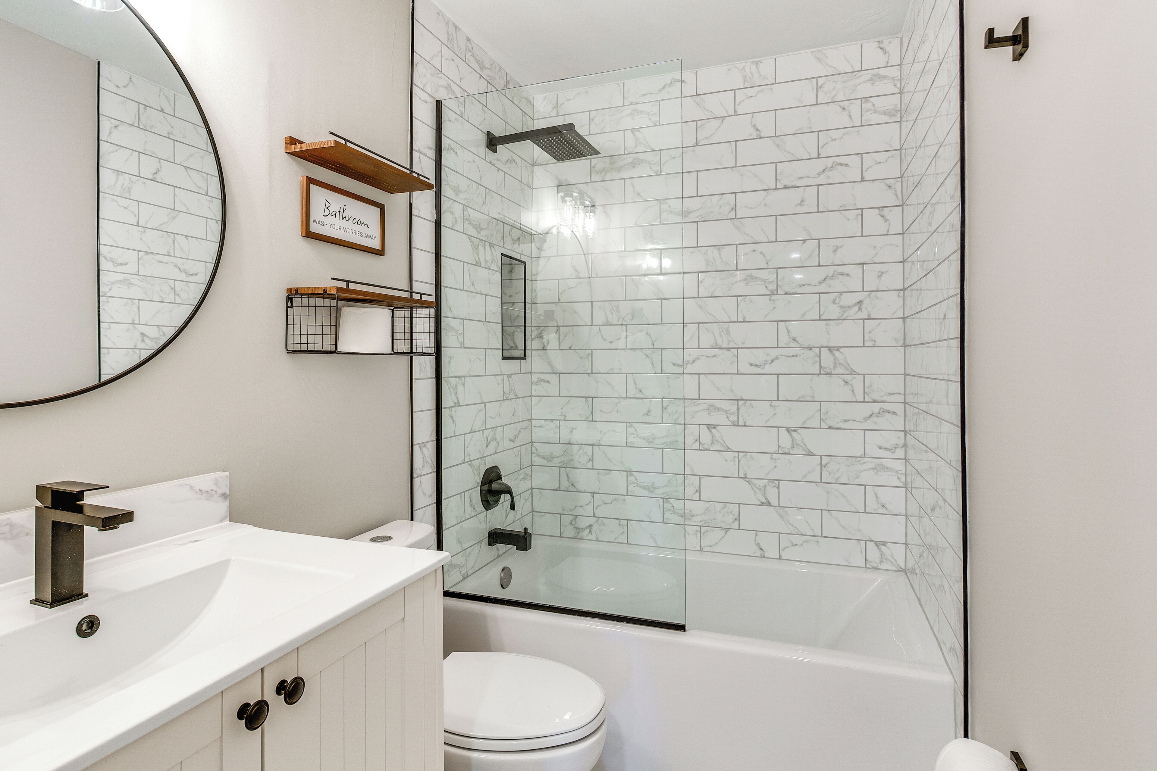 A bathroom with a white marble tile shower, a white toilet, and a white sink with a modern faucet.