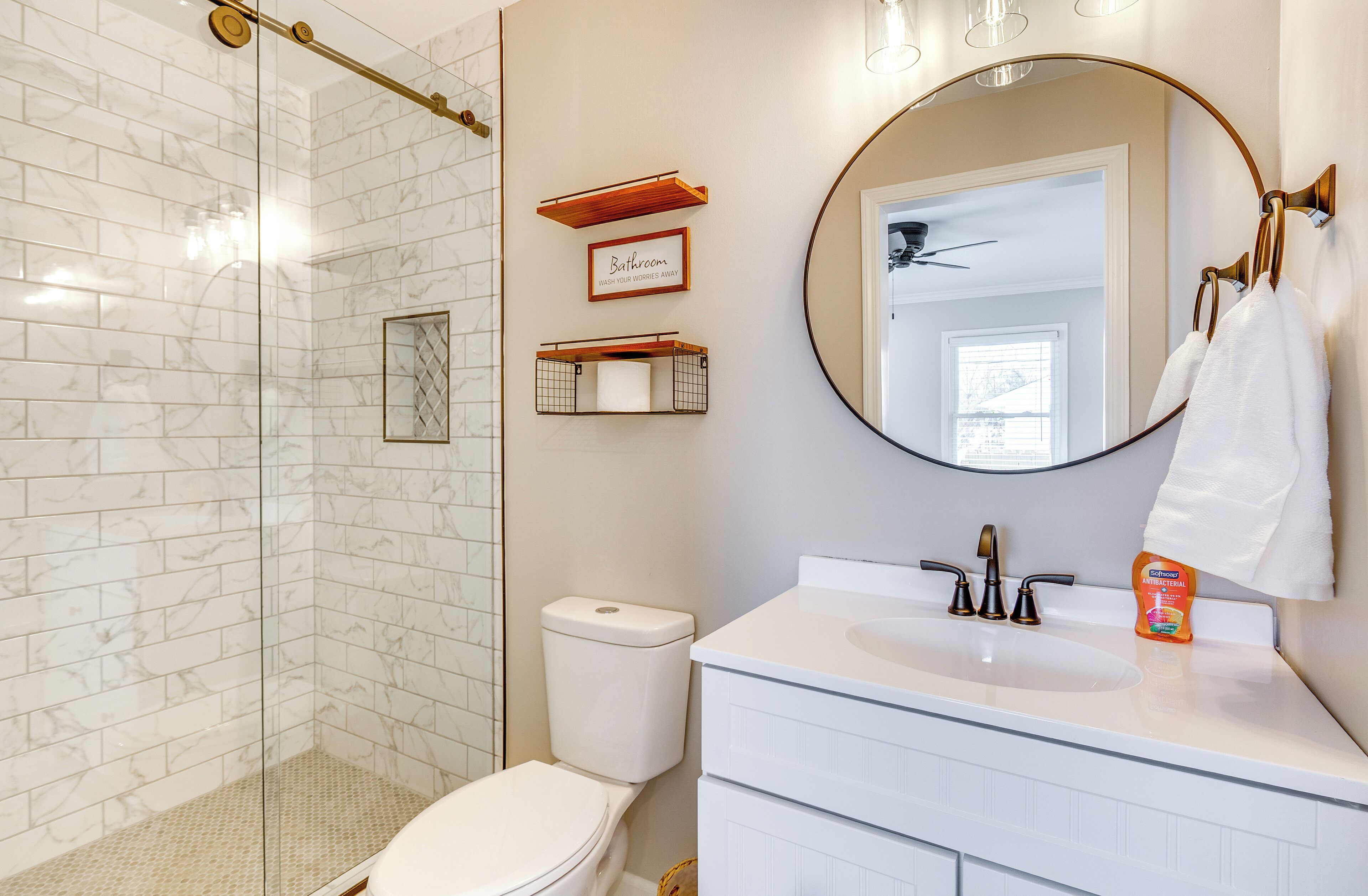 A bathroom with a glass shower enclosure, a toilet, a sink with a mirror above it, and a towel rack.
