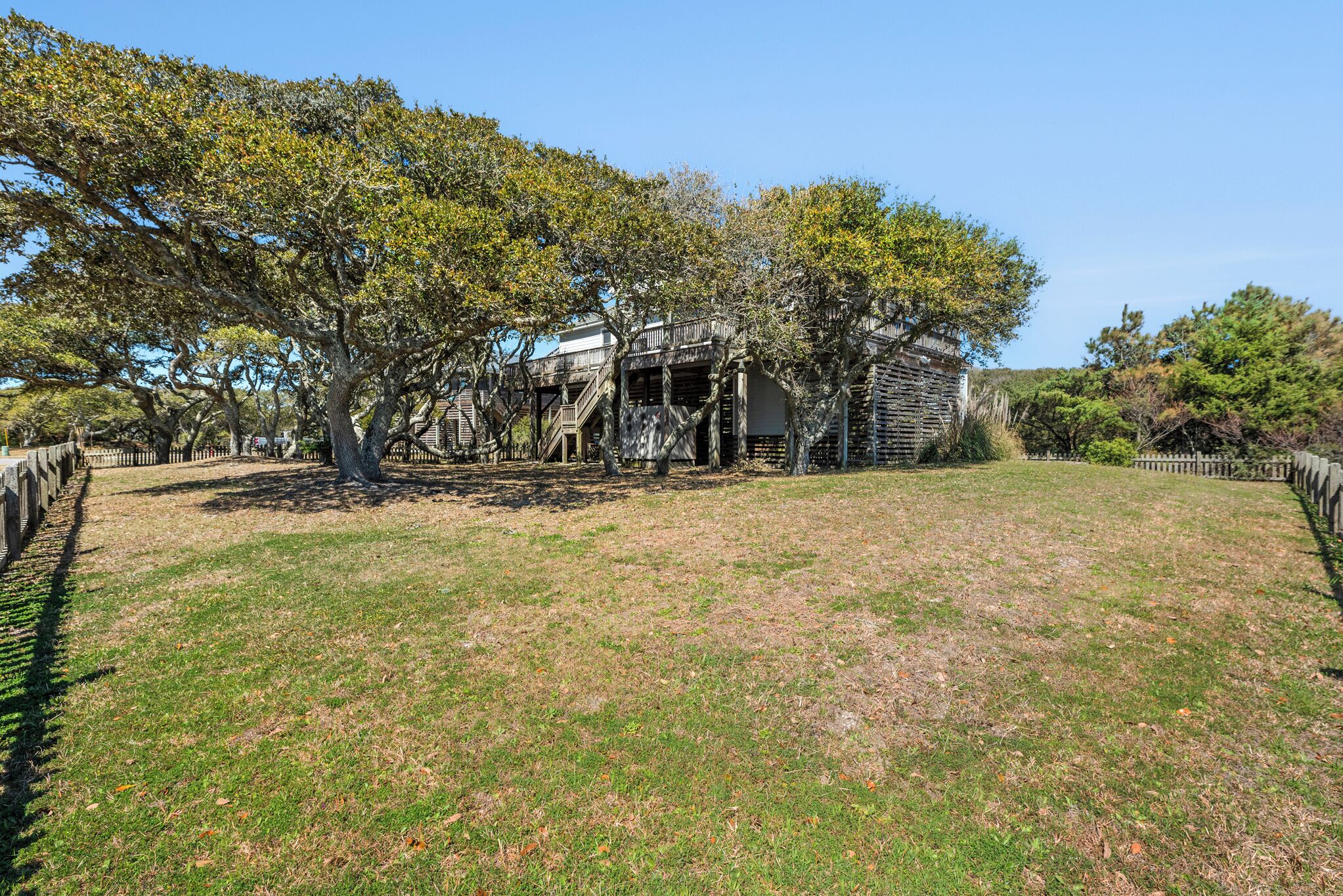 An old wooden building with a balcony, surrounded by trees and a grassy area.
