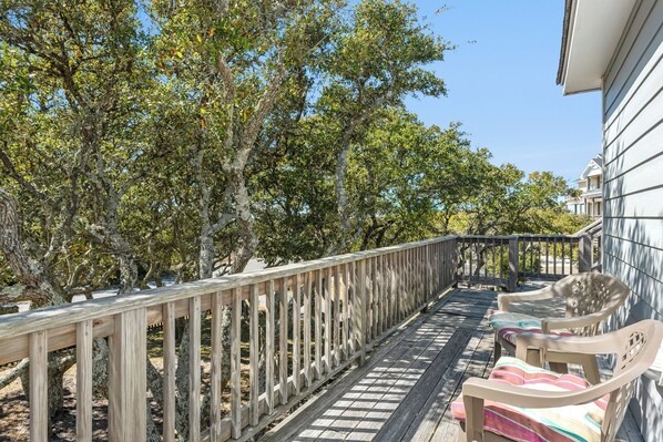 A wooden deck with a railing, two plastic chairs, and a building in the background. - Reel Heaven: Soundside | Fenced in Yard for a Dog | Walk to the Beach | (Frisco)