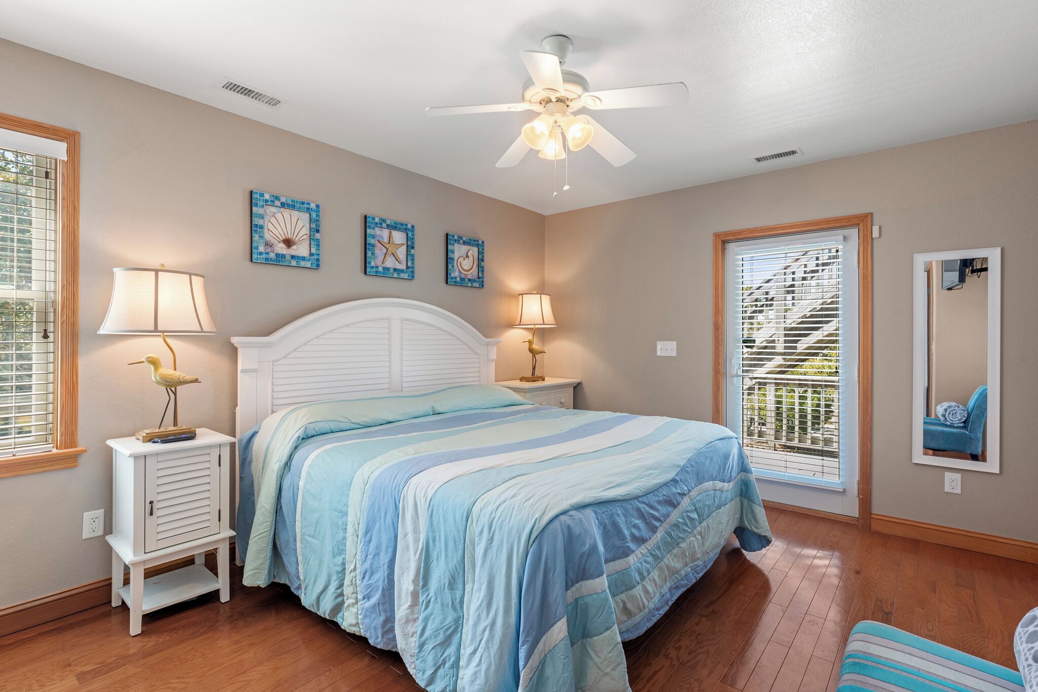 A bedroom with a bed, two bedside tables with lamps, a ceiling fan, and a window with blinds.