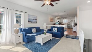 A modern living room with a blue sofa set, a white coffee table, and a ceiling fan. - Sea Escape: Semi-Oceanfront | Easy Beach Access (Kill Devil Hills)