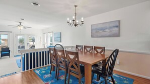 A dining area with a wooden table and chairs, a chandelier, and a painting on the wall. - Sea Escape: Semi-Oceanfront | Easy Beach Access (Kill Devil Hills)