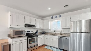 A modern kitchen with white cabinets, stainless steel appliances, and a granite countertop. - Sea Escape: Semi-Oceanfront | Easy Beach Access (Kill Devil Hills)