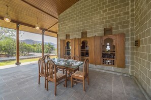 A covered patio with a table and chairs, wooden cabinets, and a view of greenery and hills.