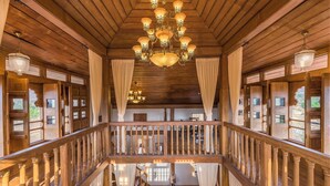 A wooden interior with a grand chandelier, wooden railings, and large windows. - CosmicStays Parambi Farm- Vintage Charm  (Bhor)