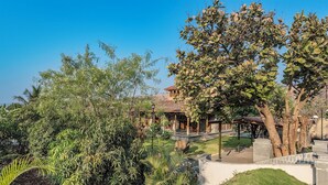 A courtyard with a gazebo, a building with a tiled roof, and various trees and plants. - CosmicStays Parambi Farm- Vintage Charm  (Bhor)