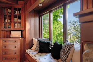 A wooden room with a built-in bench, a cabinet with glass doors, and a window with a view of trees.