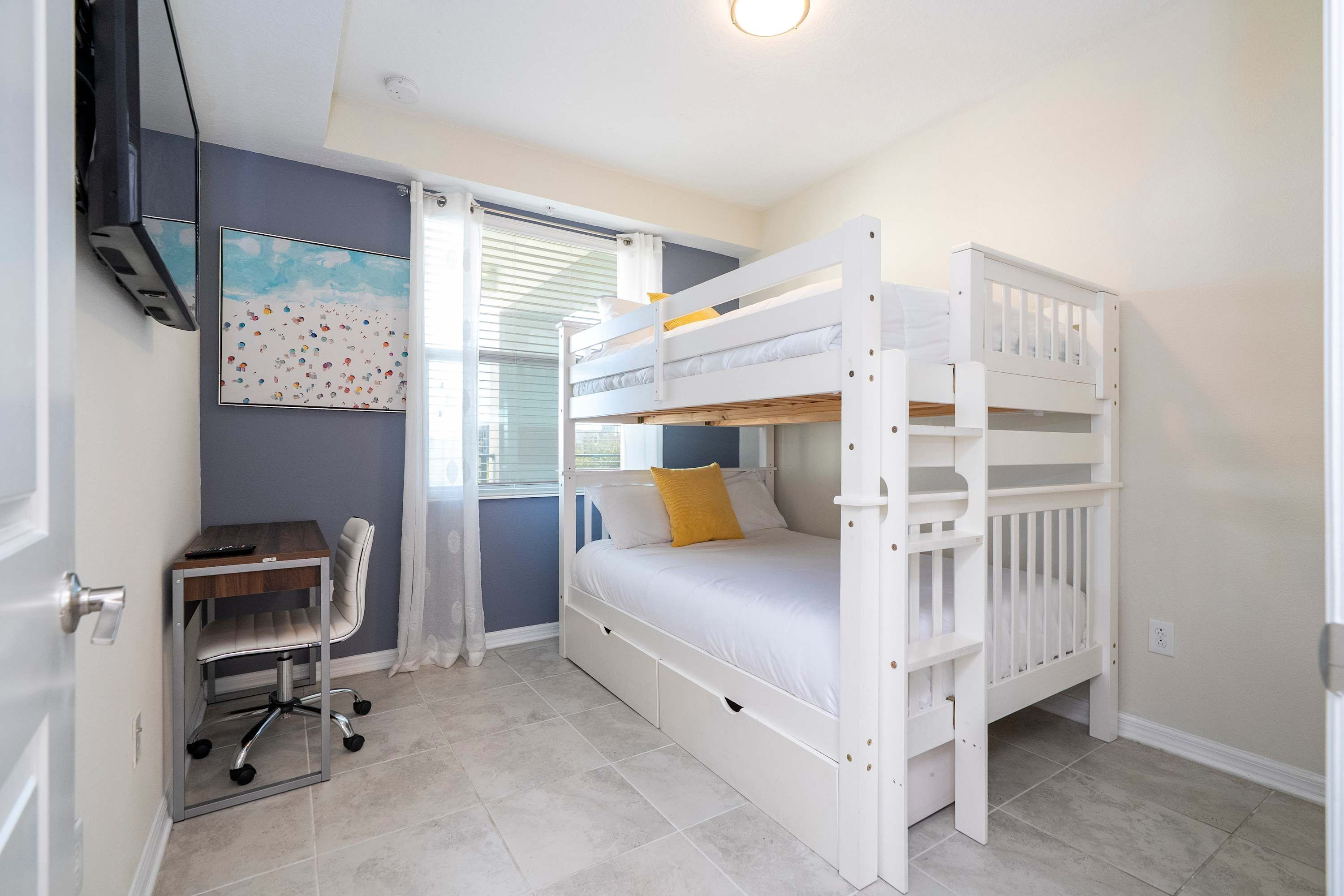 A bedroom with a bunk bed, a desk with a chair, and a window with blinds.
