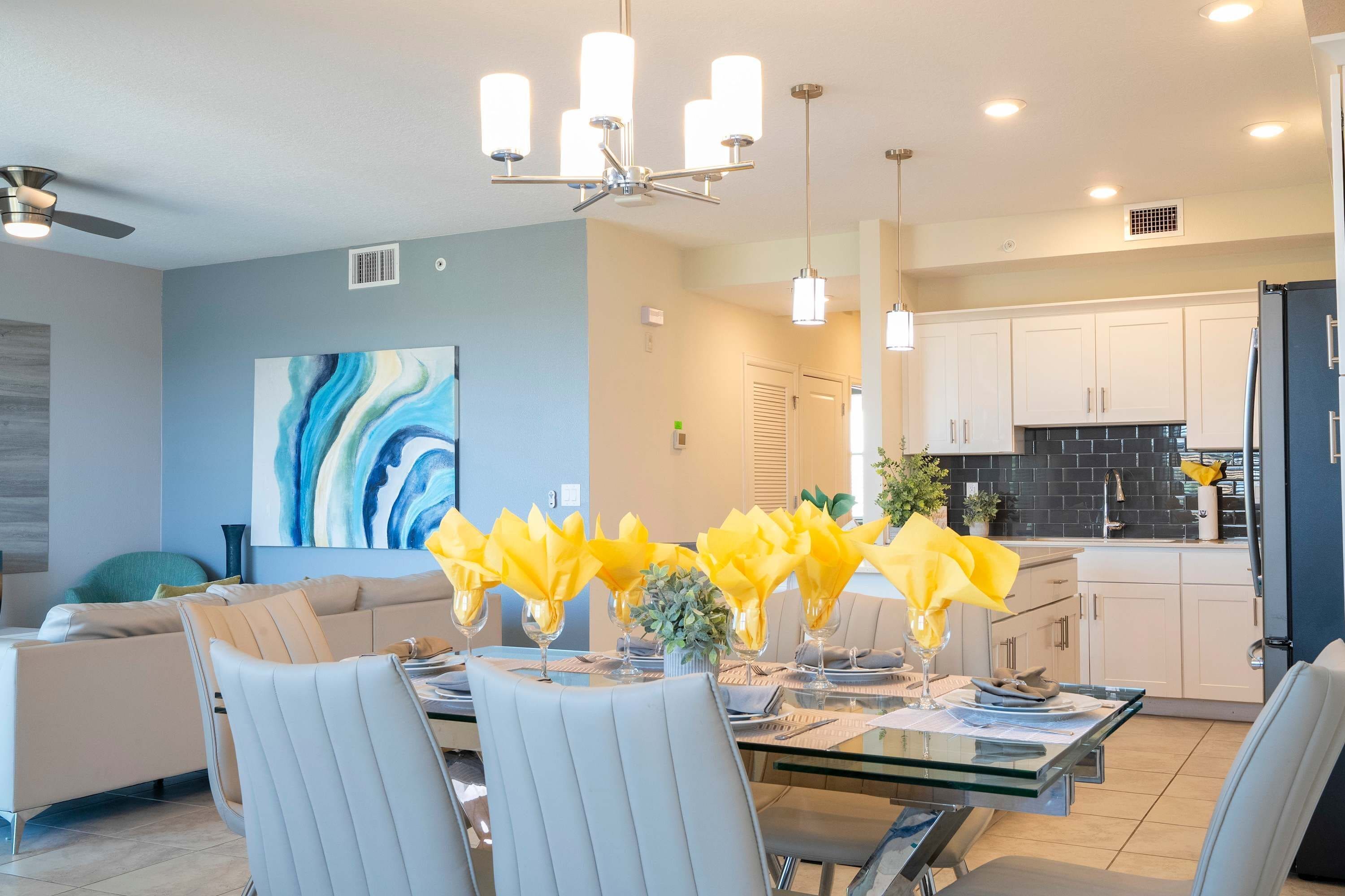 A modern dining area with a glass table, white chairs, and yellow napkins.