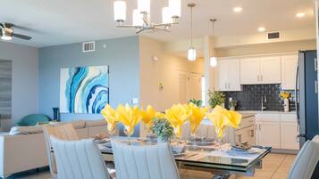 A modern dining area with a glass table, white chairs, and yellow napkins.