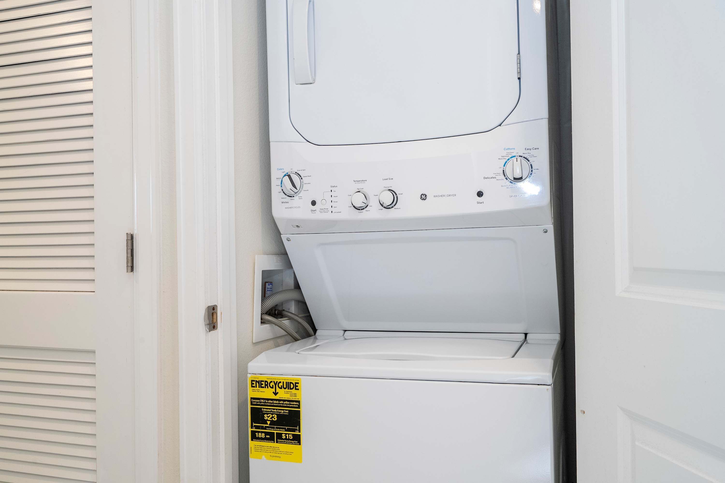 Vue de face d’un appareil combiné lave-linge et sèche-linge à chargement frontal, de couleur blanche, avec un panneau de commande, une étiquette jaune indiquant le niveau de rendement énergétique et un tuyau d’évacuation visible sur le côté gauche.