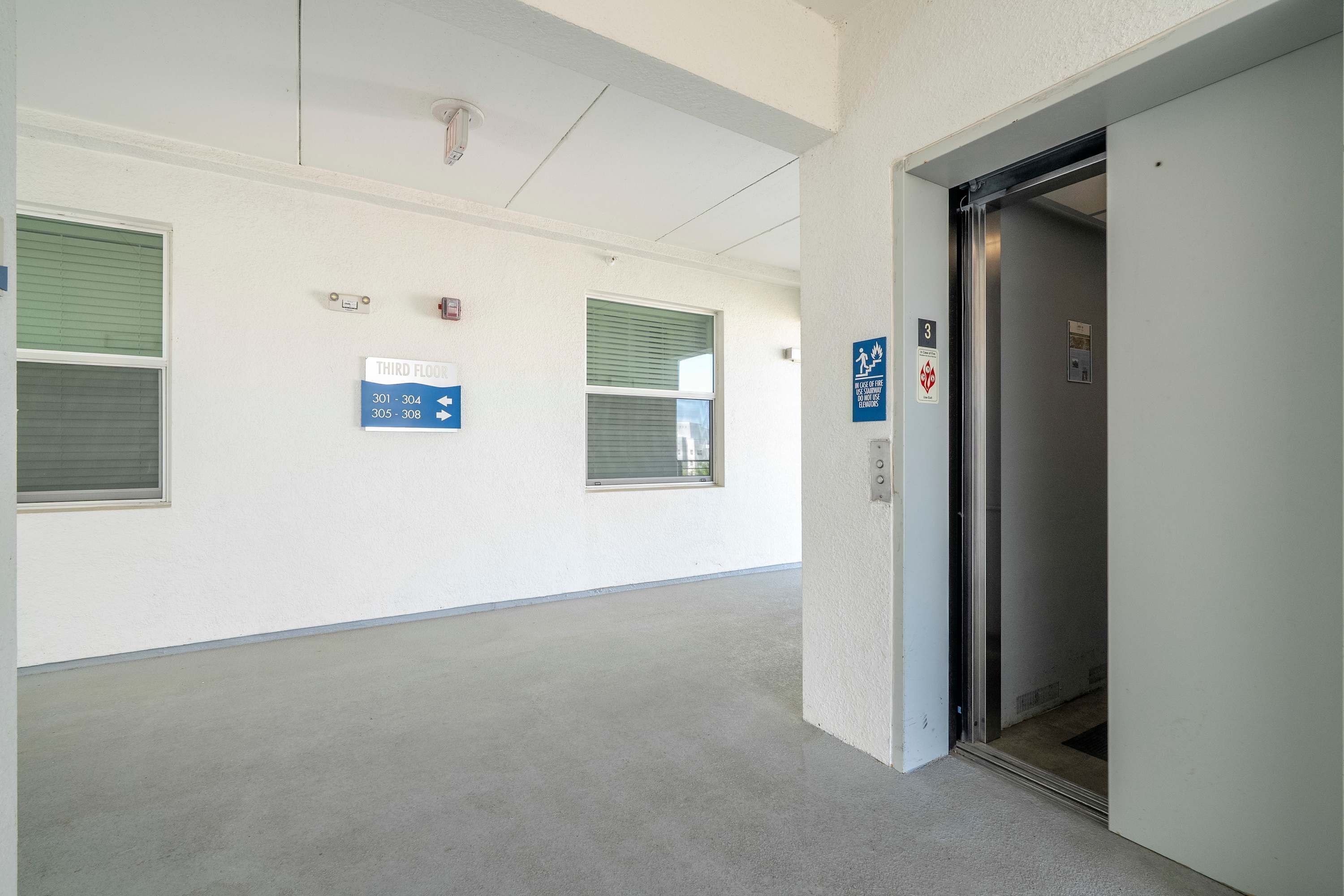 Un corridoio con una insegna che indica il terzo piano, un allarme antincendio e la porta di un ascensore.