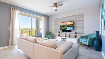 A modern living room with a sofa, two chairs, a TV, and a ceiling fan.