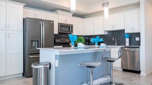 Una cocina moderna con armarios blancos, electrodomésticos de acero inoxidable, una isla central con taburetes y una planta en maceta.