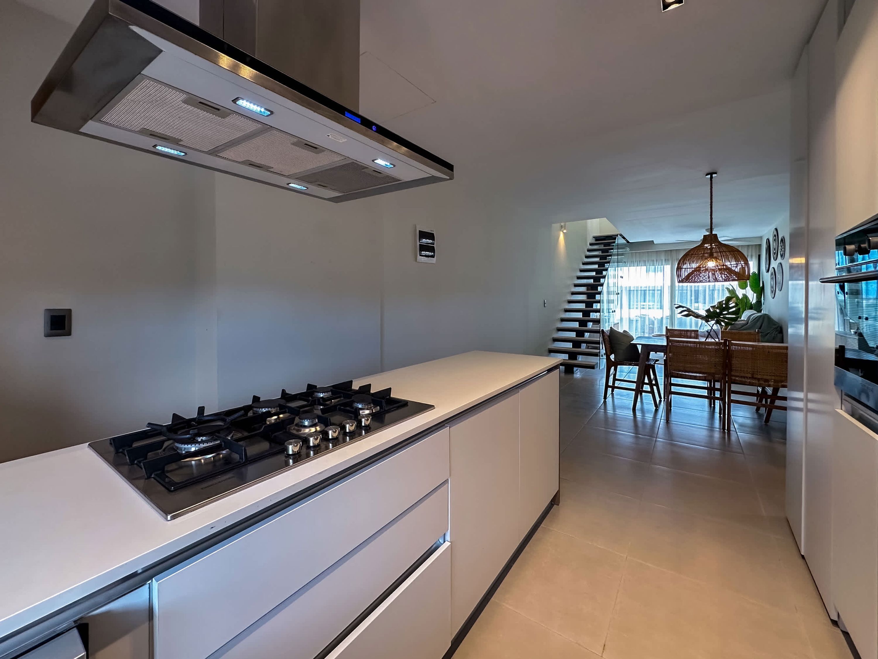 Een moderne keuken met een centraal eiland, roestvrijstalen apparatuur en een trap naar een eetruimte met uitzicht.