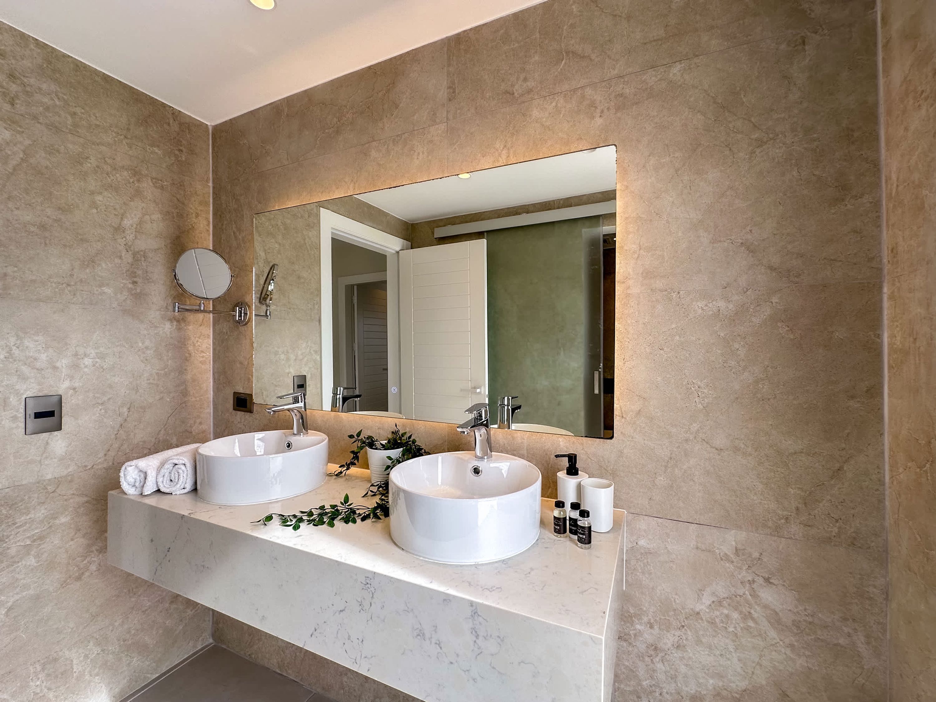 Une salle de bain moderne avec deux vasques, un grand miroir et un plan de toilette en marbre.